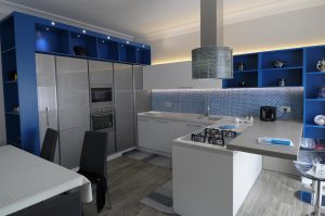 Cucina contemporanea blu, bianco e grigio, lucida e brillante, ben strutturata ed equipaggiata da elettrodomestici moderni ed all